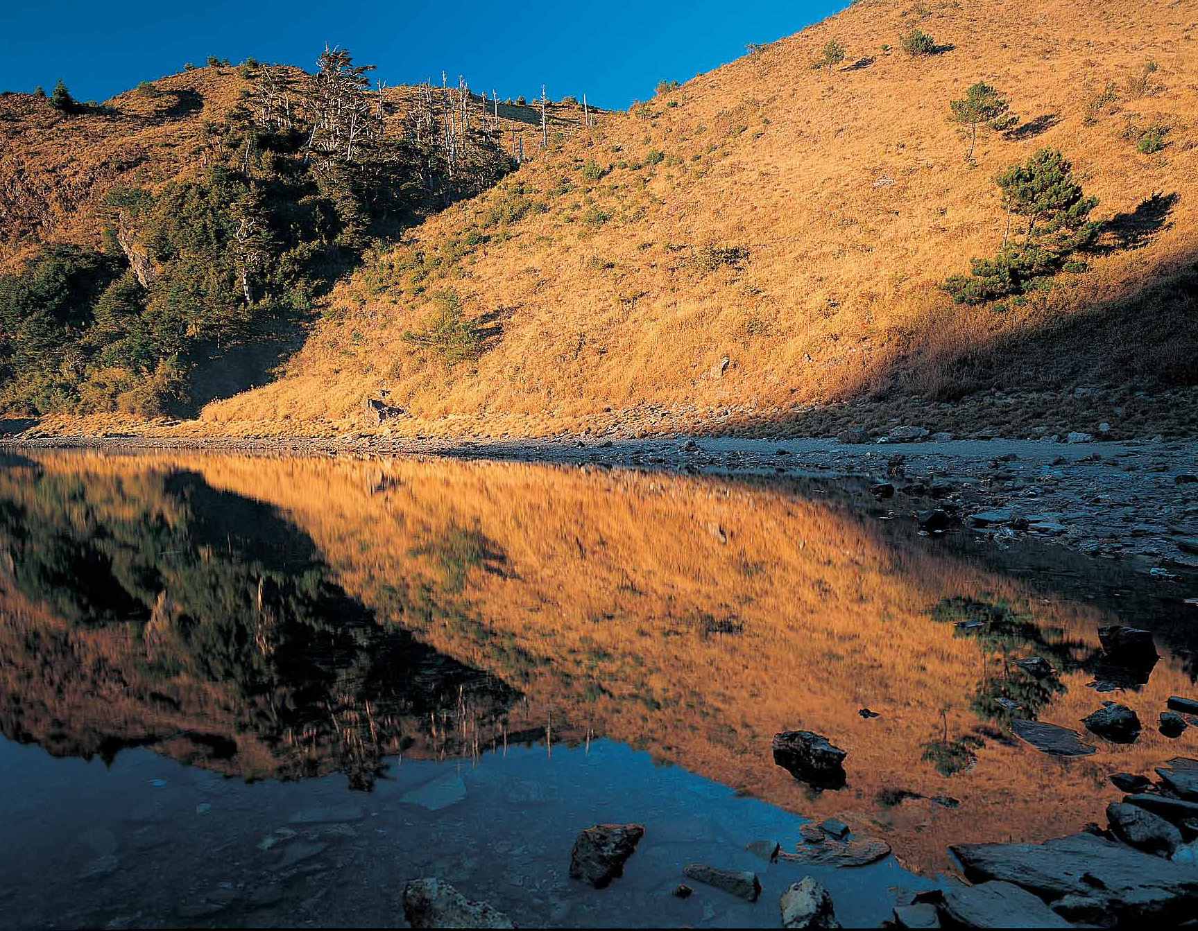 晨光像刺目的火焰照亮了山頭，倒映在平如明鏡的湖面，營造出夢幻的情境。
