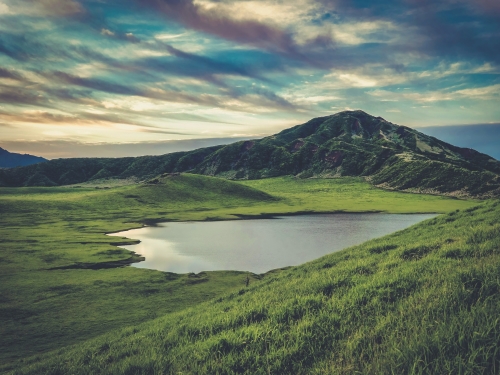 位於阿蘇九重國立公園的千草里之濱／ Kohji Asakawa提供（ 圖片來源：https://unsplash.com/photos/green-grass-field-near-lake-under-cloudy-skyduring-daytime--oXgLqhQ4NI）